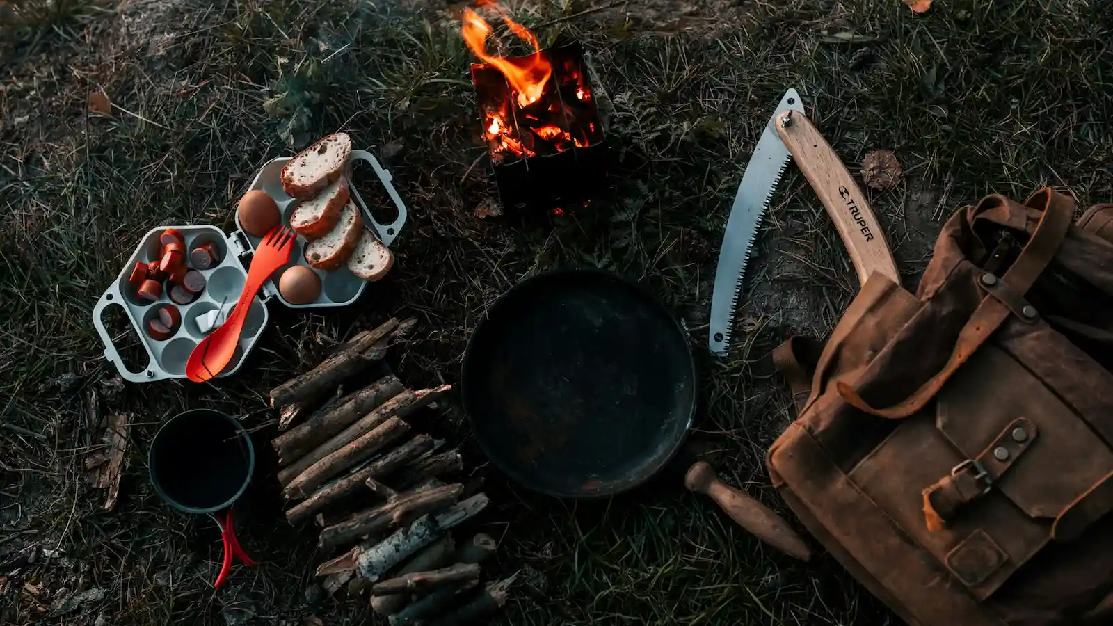 Bushcraft-Ausrüstung mit Lagerfeuer, Pfanne und Säge – Symbolbild für Bushcraft Grundskills