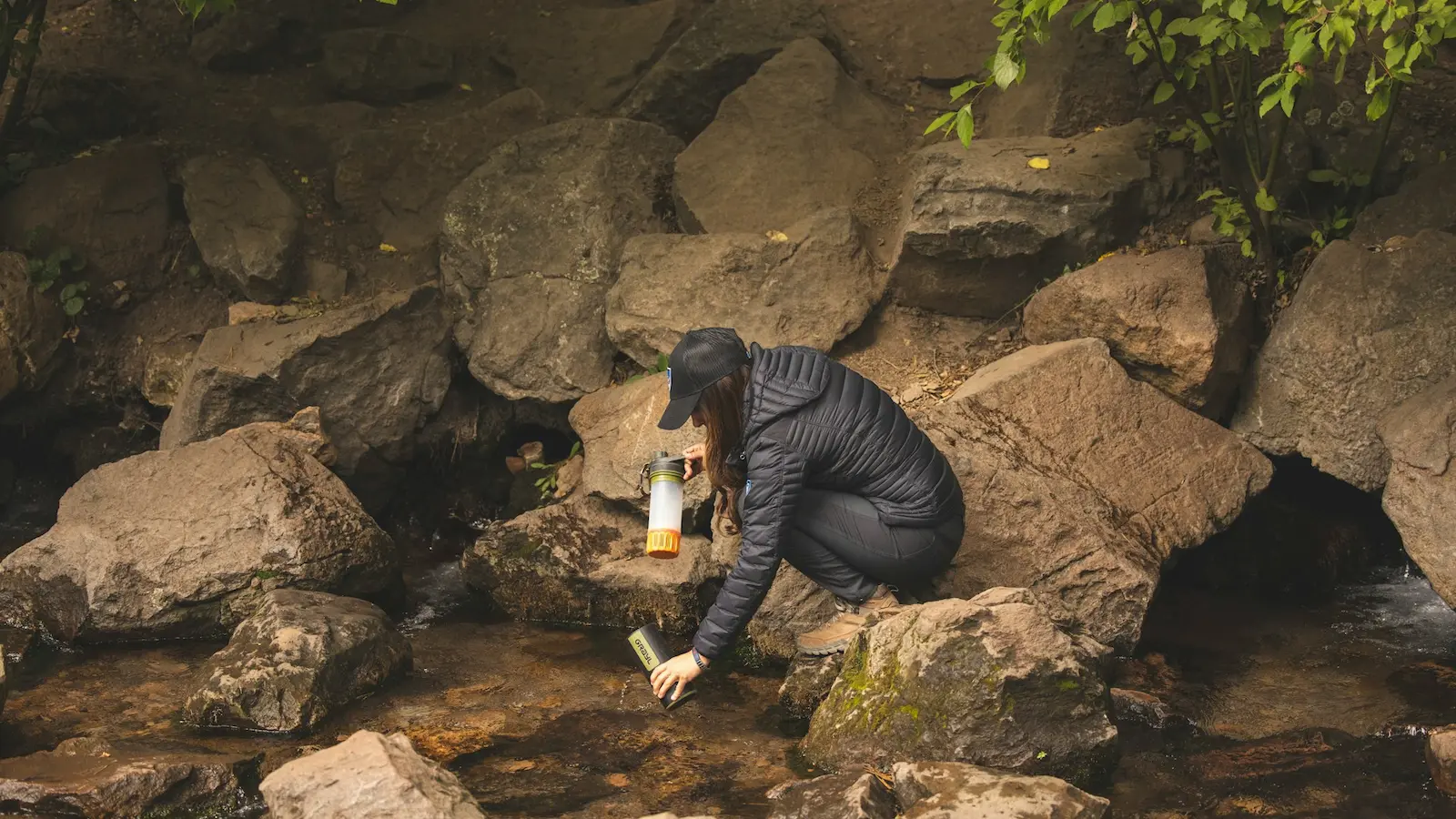 Person füllt Wasserfilter an einem Gebirgsbach – Wasser filtern in der Wildnis